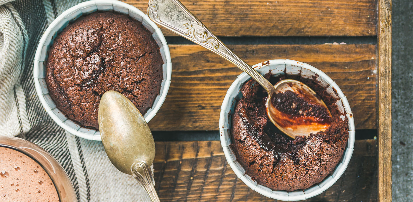 Two dishes of souffle with spoon in them on a wooden table.