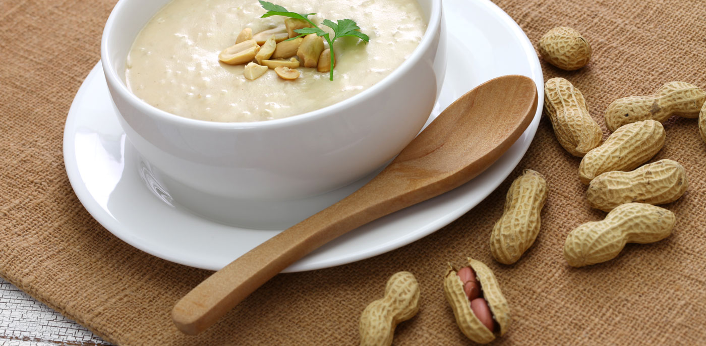 White bowl full of Thai Peanut Soup topped with peanuts.