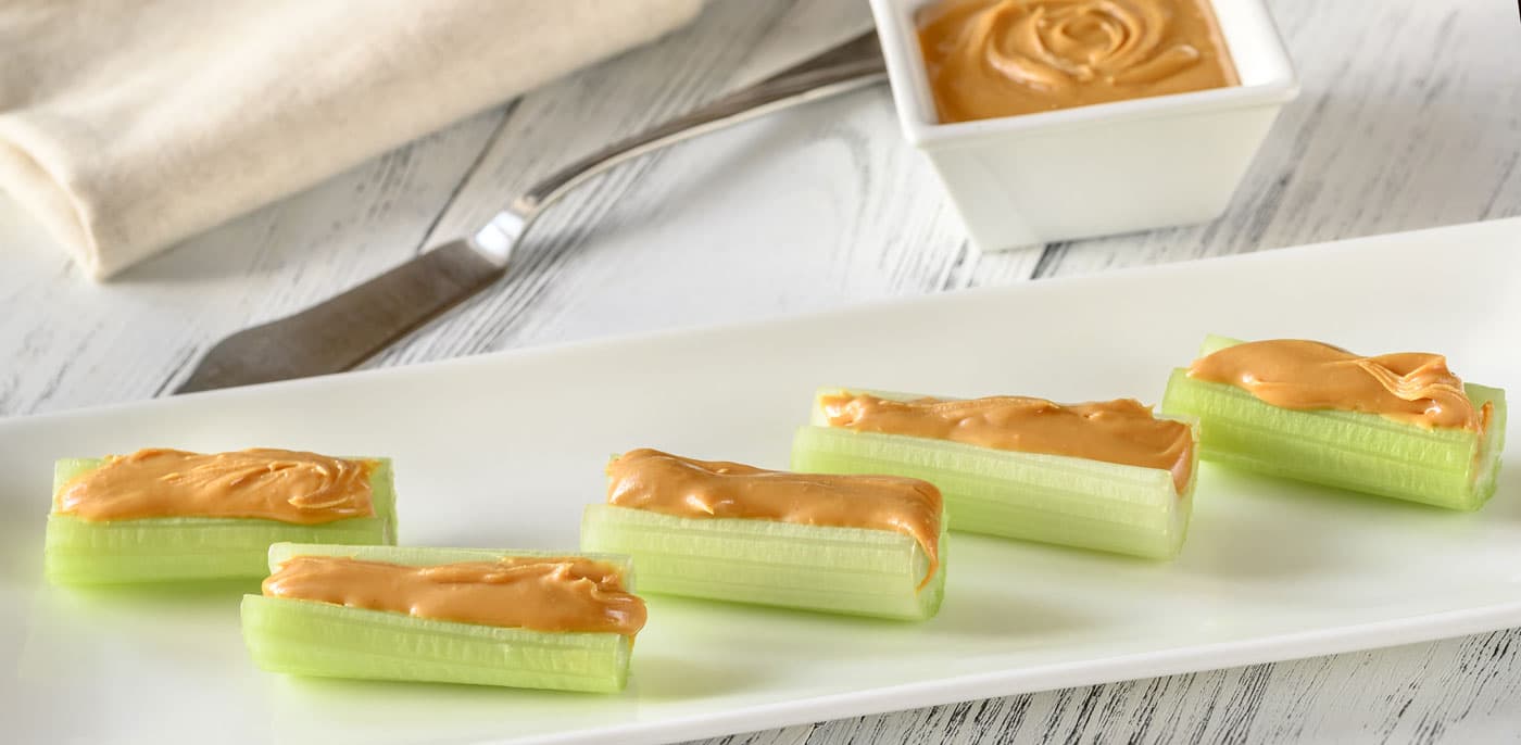 Sticks of celery filled with peanut butter on a white plate