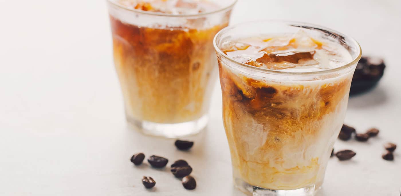 Two glasses of iced coffee with coffee beans scattered nearby