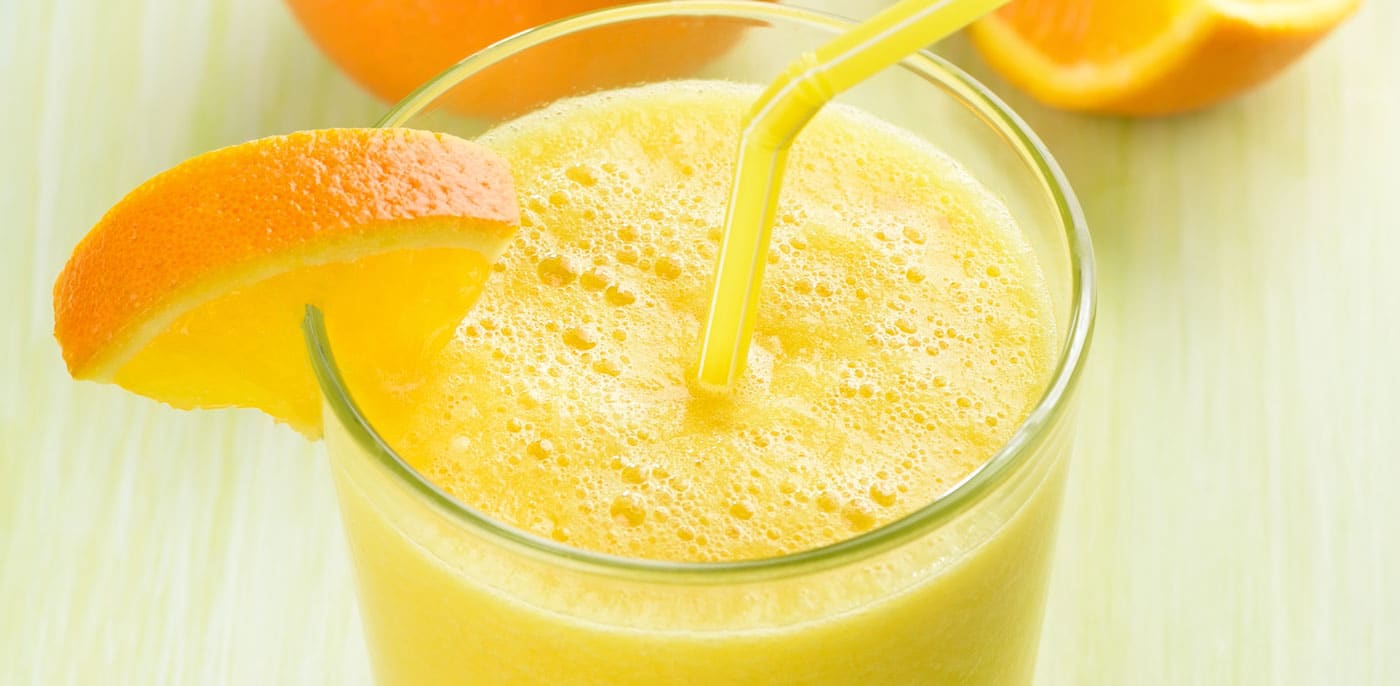 Tall glass of orange juice with an orange wedge of the rim