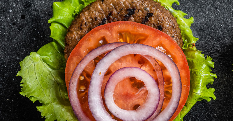 Burger patty on lettuce with tomato and red onion.
